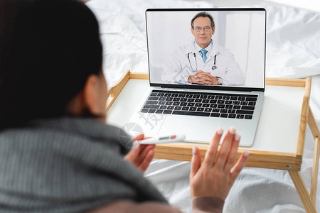 在笔记本电脑上与男医生进行在线咨询的患有疾病的妇图片