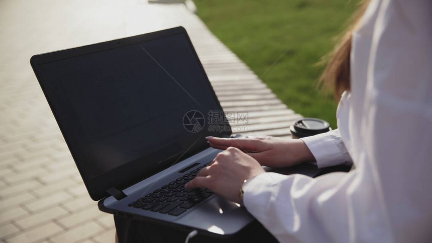 年轻商业妇女坐在户外用笔记本电脑打工图片