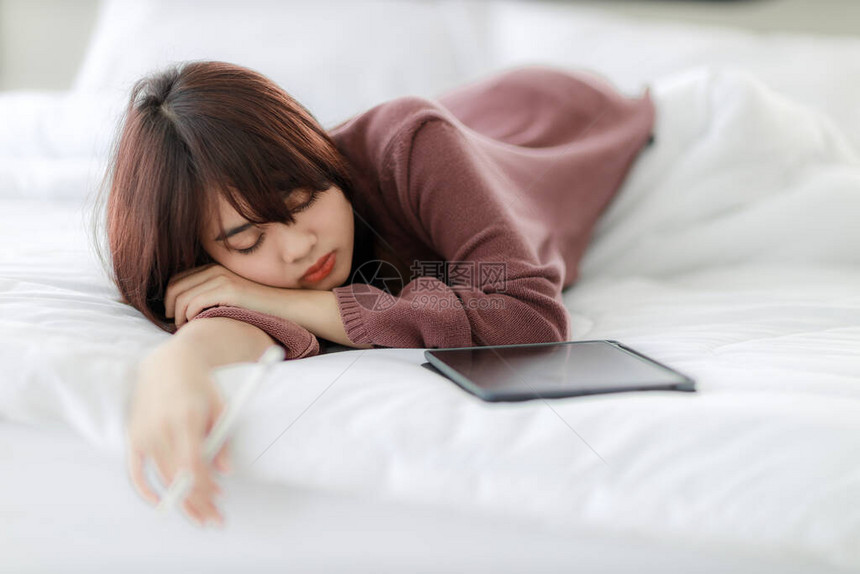 亚洲女在床上睡觉和使用平板电脑进行工作教育电子商务社交媒体图片
