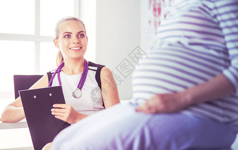 在医院与孕妇使用听诊器和药片的年轻女医生图片