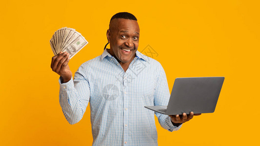 现金返还和网上购物的概念兴奋的成熟非洲裔美国人拿着很多钱和笔记本电图片