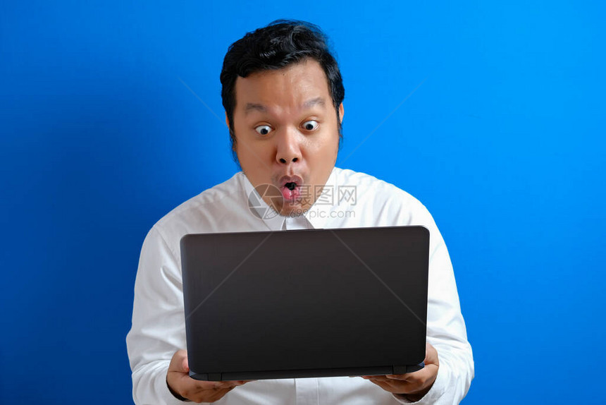 年轻亚洲商人穿着随身穿白衬衫看笔记本电脑惊讶的表情图片