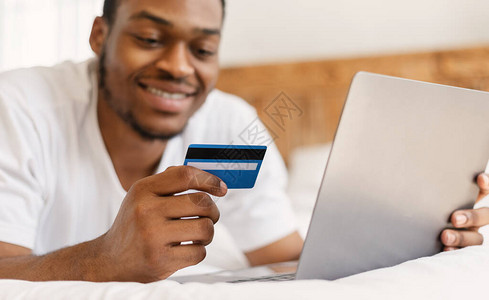 周末在家躺在床上用笔记本电脑和信用卡做网上购物的黑人图片