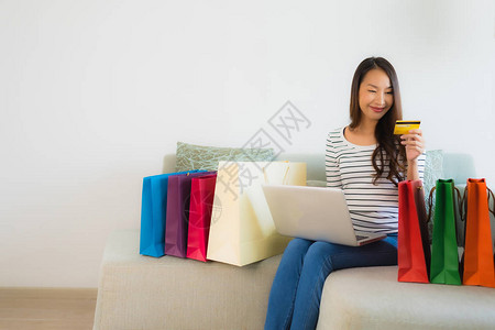 用信卡手机或电脑在客厅内的沙发上在线购物的美丽亚洲图片