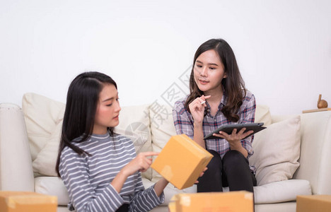 两个亚洲女包装产品和用平板检查小办公室网上购物和电子商务客户的订单图片