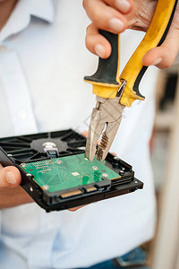 女使用黄色金属钳子修补残废生产HDD磁盘驱动器拆卸绿板的破碎穷人的图片