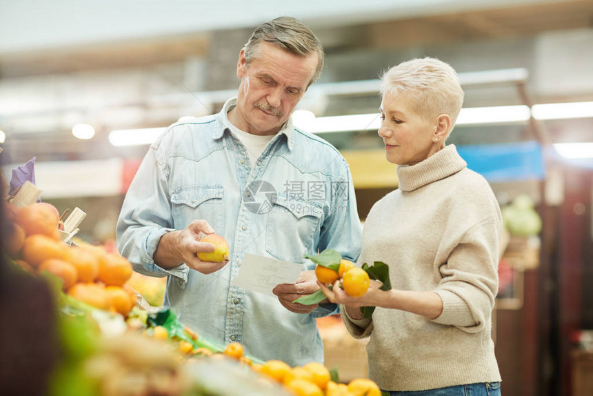 现代老年夫妇在当地农贸市场购物时选择柑橘类水果的画图片