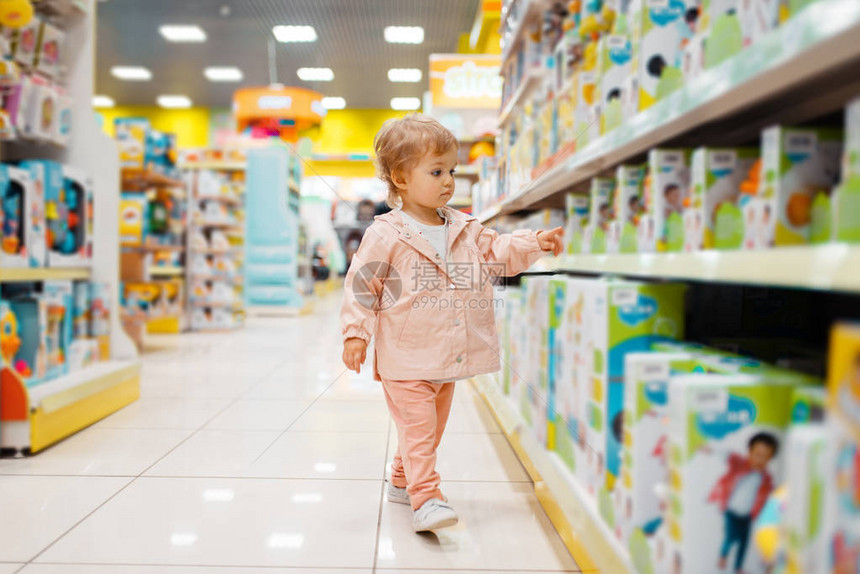 在书架上的小女孩在儿童商店旁观的侧面选择玩具女儿在超市家庭购图片