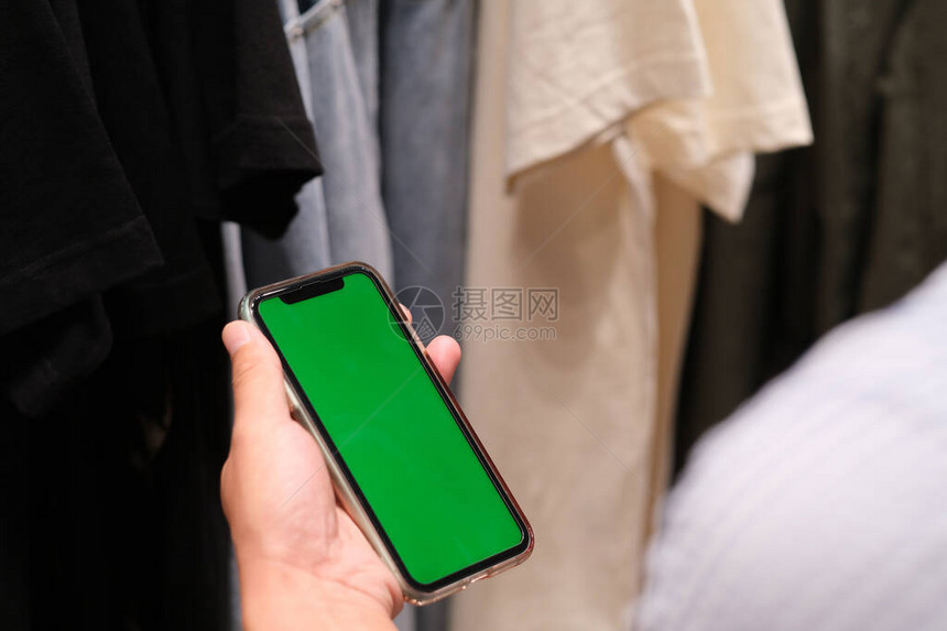 握着绿色屏幕智能电话在许多衣服面图片