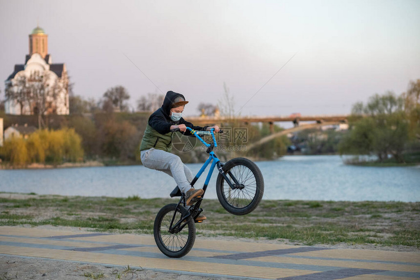 一个戴面罩的青少年骑着一辆蓝色黑自行车在后轮上行驶图片