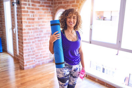 在健身房上瑜伽前站着拿运动垫子和一瓶水喝着呢图片