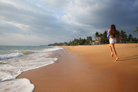 快乐的女孩在海洋的沙滩上快乐地奔跑和跳跃图片