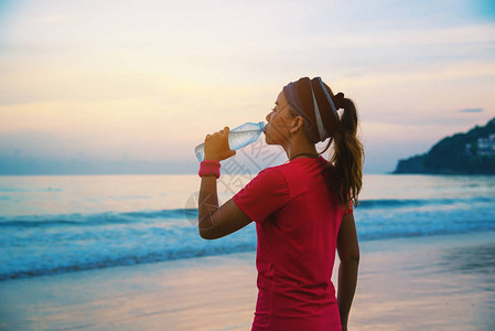 请您喝水亚洲妇女早上在海滩上慢跑锻炼您可以在海边散步和用塑料瓶喝水来放松身心海滩运动锻炼背景