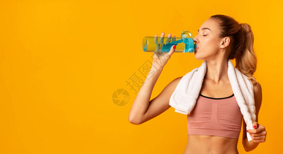 补水健身妇女在锻炼期间站在工作室的黄色背景上喝水有空图片