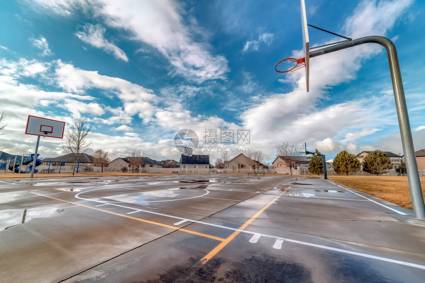 在邻里公园的篮球场与房子和操场在背景中美丽的蓝天下的住图片