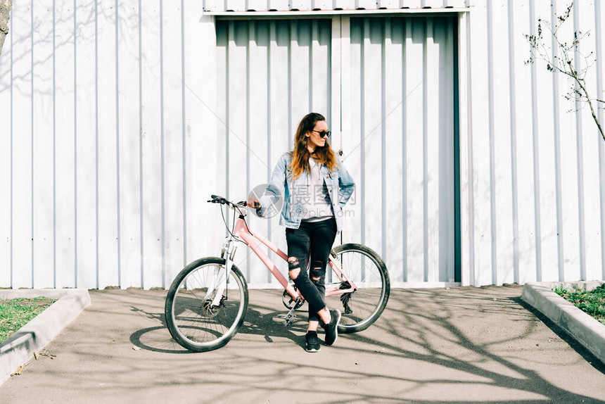 一个年轻时尚的女孩坐在她旁边的一辆粉红色自行车在轻光机图片