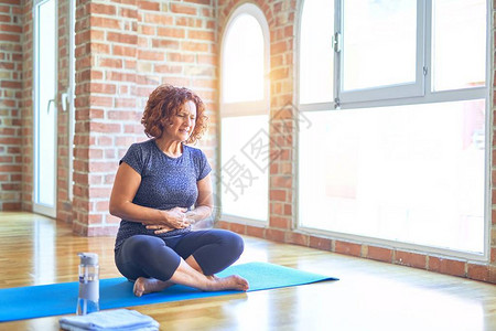 中年美女运动员穿着运动服坐在垫子上在家练习瑜伽图片