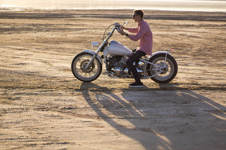 日落时在沙漠路上驾驶摩托车的年轻图片