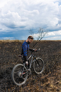 在烧毁的田野上骑山地自行车的大胡子自行车手图片