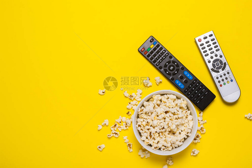电视电视调谐器和黄色背景上的一碗爆米花的两个遥控器概念系列电影体育横幅图片
