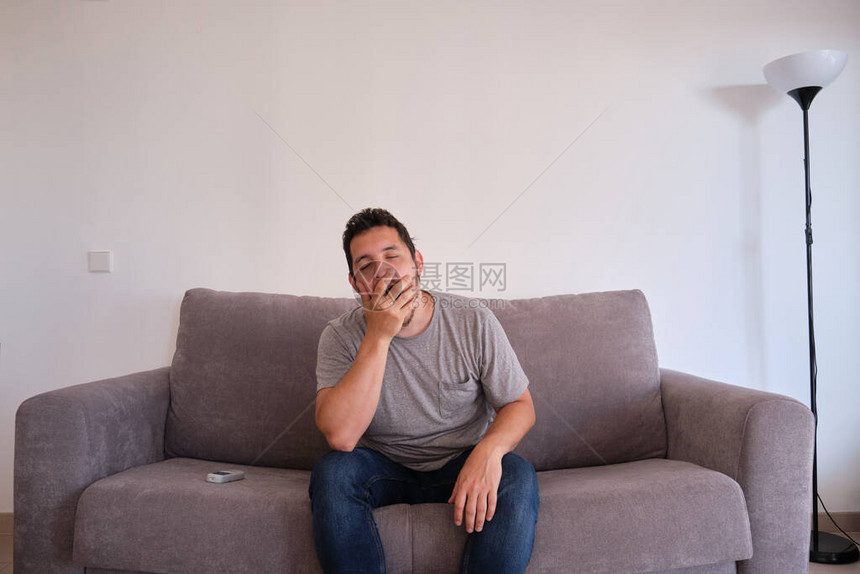 一个无聊疲劳的年轻人坐在沙发上打哈欠时的肖像法蒂格图片