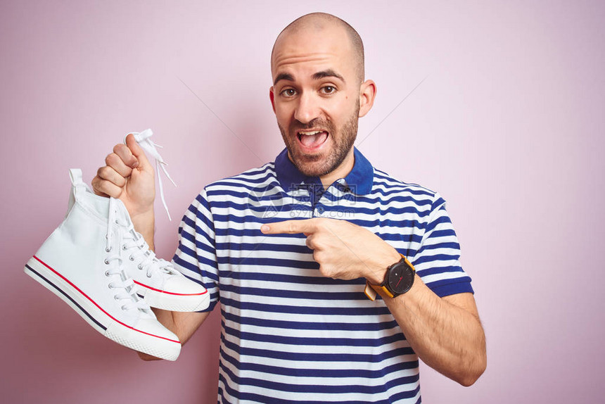 在粉红孤立背景上穿着随意运动鞋的青年男子非常快乐地用手和图片