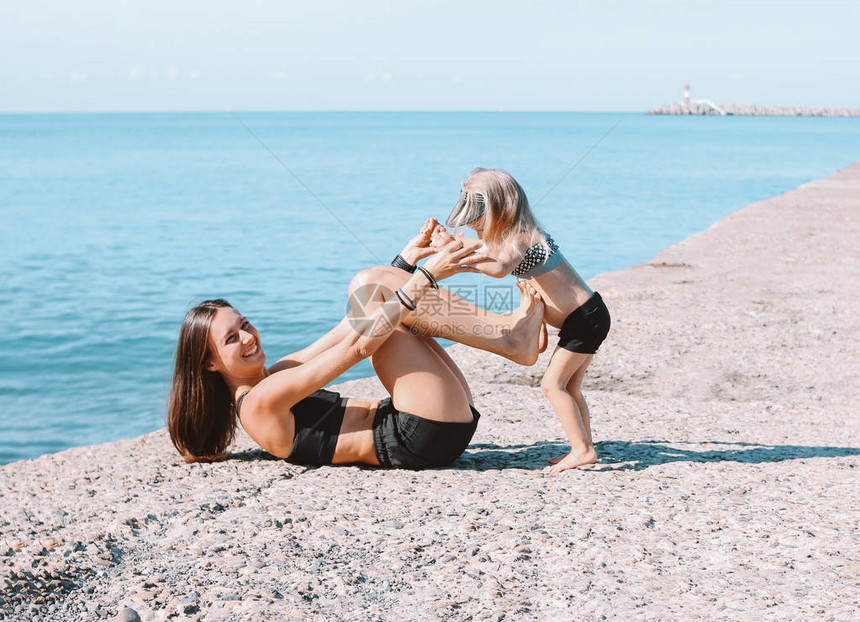 年轻健康的女妈和可爱的小女孩一起在沙滩上锻炼图片