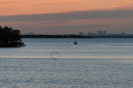 在日出时清晨金色时分一艘游艇驶过湖面与附近城市的树木和建筑相隔图片