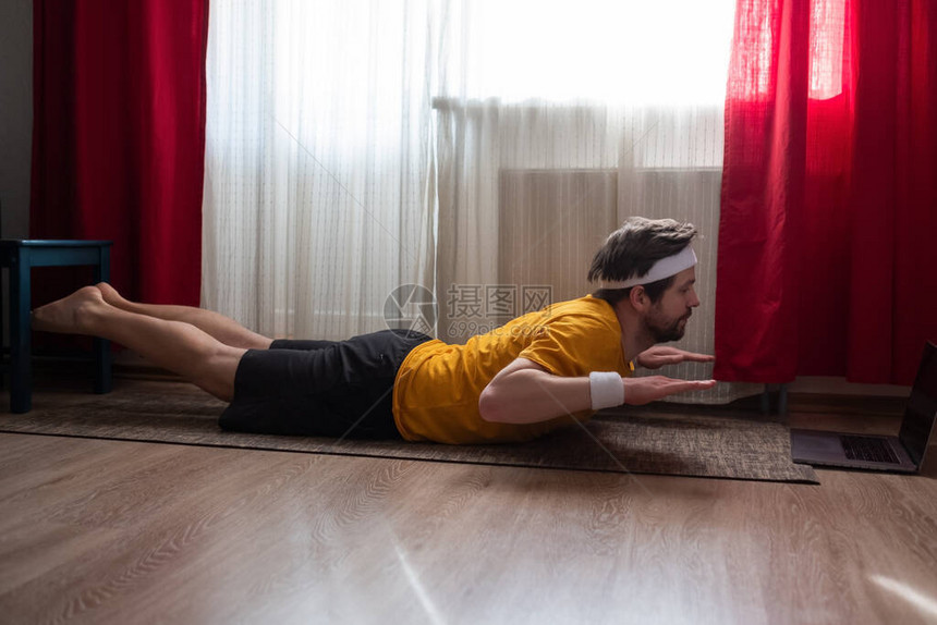 有运动肌肉的年轻瑜伽男在家中客厅做后背式SalabhasanaLocustPos图片