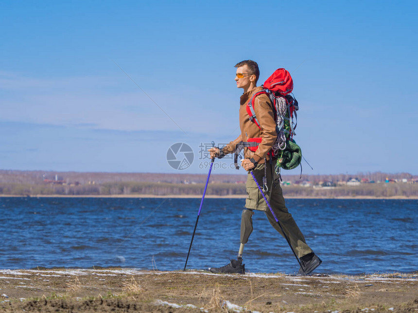 一个带着假肢的人在河边行走的侧面图背着包的北欧行走积极的生活方式动图片