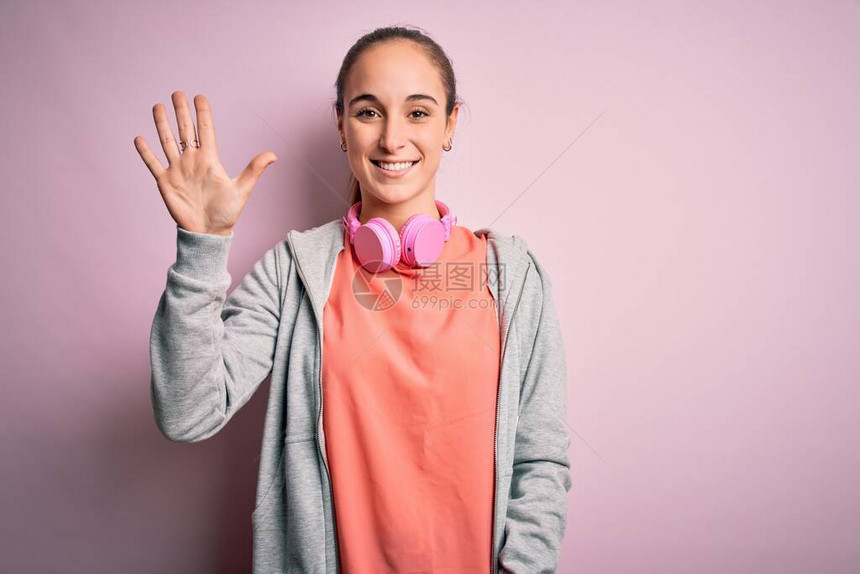 美丽的运动型女人在做运动时使用耳机在粉红色的背景上听音乐图片