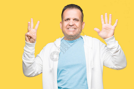 身穿运动衫的中年阿拉伯男子在孤立的背景下展示并用八号手指向上方图片
