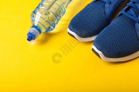 蓝色运动鞋和黄色背景上的一瓶水健康生活方式日常训练和图片