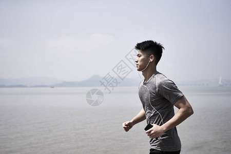 年轻的亚洲成年男子在海边慢跑侧视图图片