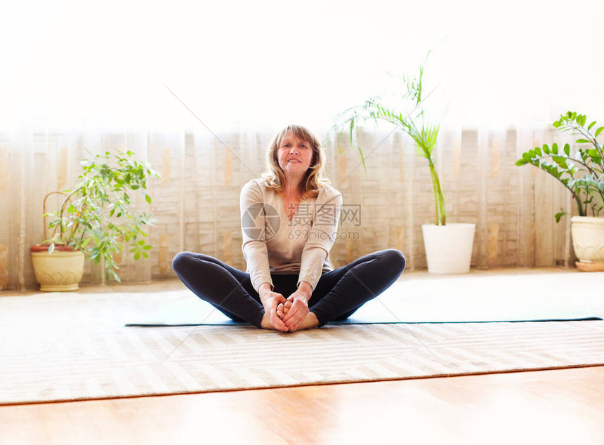 坐在蝴蝶地板上全身赤脚裸足的老年女在家中宽敞的房间做瑜伽时图片