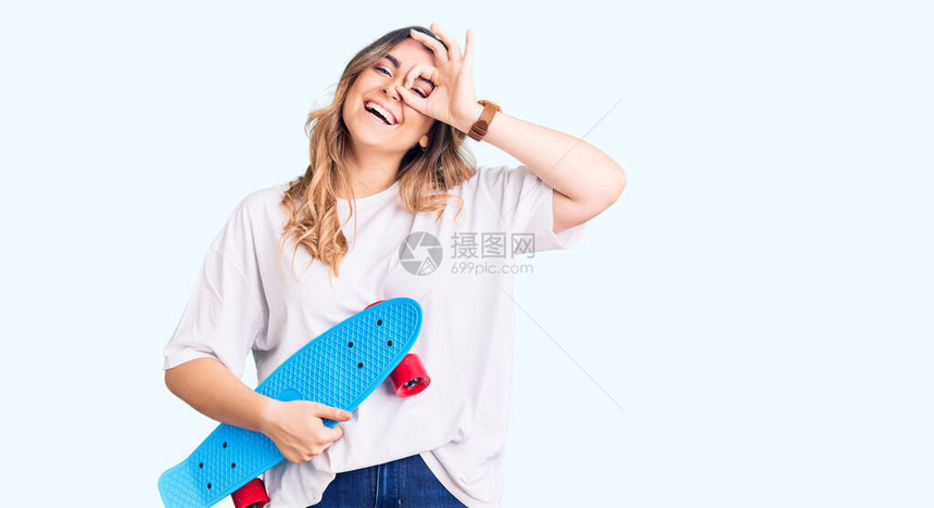 年轻的白种女人拿着溜冰鞋微笑着开心地做着好手势图片