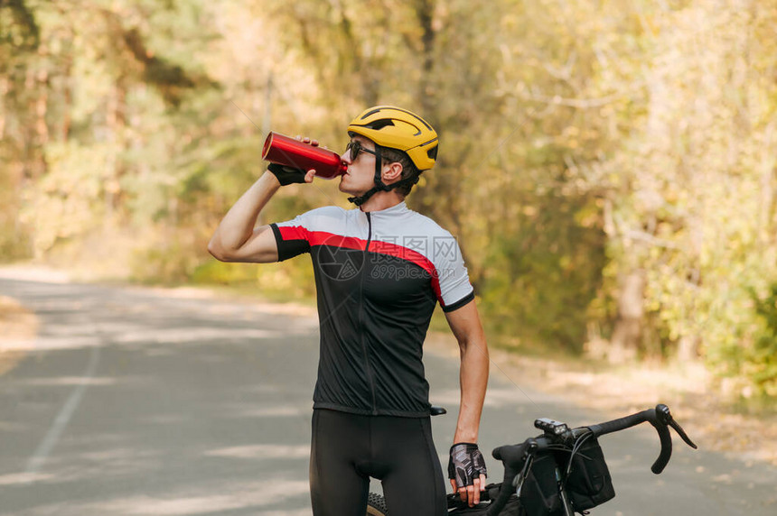 一位穿着运动服的口渴骑自行车的人站在外面的路上图片