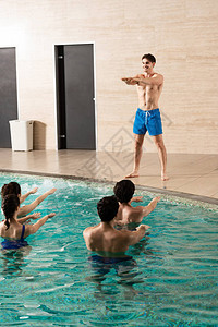 英俊的教练在与游泳池中的一群人一起训练水有图片
