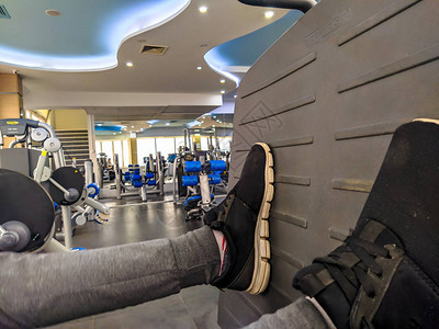 在健身房锻炼时紧男人的腿然后在健身房里做运动推着一个平台来增图片