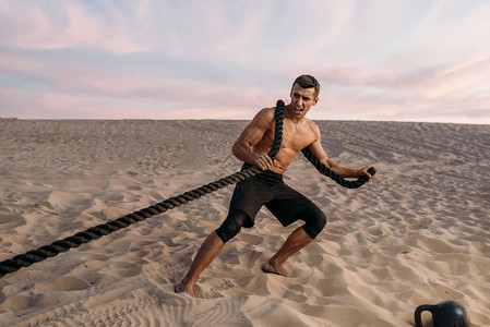 在阳光明媚的白天用绳子在沙漠中锻炼的肌肉人运动体力户外训图片