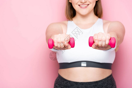 微笑的超重女孩用粉色哑铃锻炼的剪影图片
