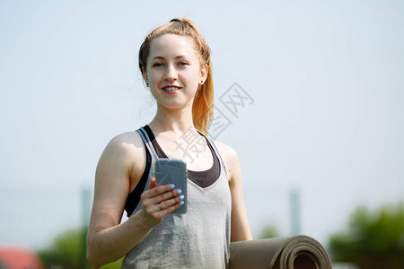 笑得可爱的年轻女子穿着运动服使用智能手机和图片