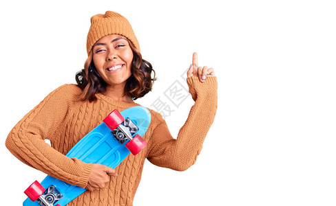 年轻美丽的混合种族女子穿着溜冰滑惊讶于一个想法或问题用快乐的笑脸指图片