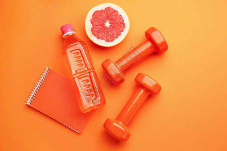 带笔记本葡萄柚和彩色背景瓶水的哑铃图片