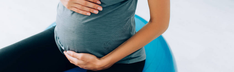 孕妇坐在健身球上时触摸肚子的图片