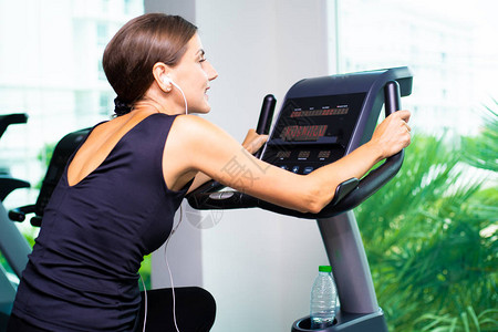 在女的健身馆锻炼自行车有氧运动女在耳机上听音乐运动员建造者图片