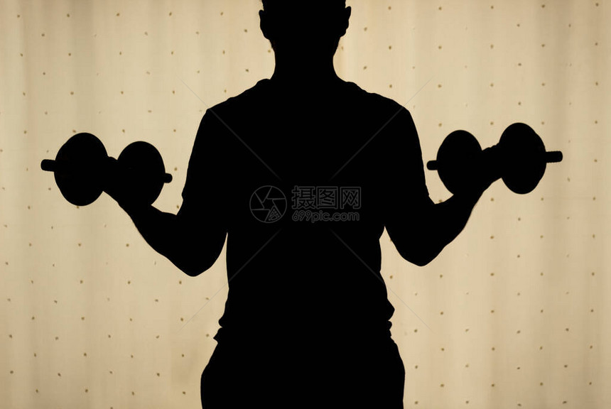 一个后面的年轻人用黄色窗帘做二头肌哑铃卷曲的剪影在背景非常适合健身运动家庭锻炼室内锻图片