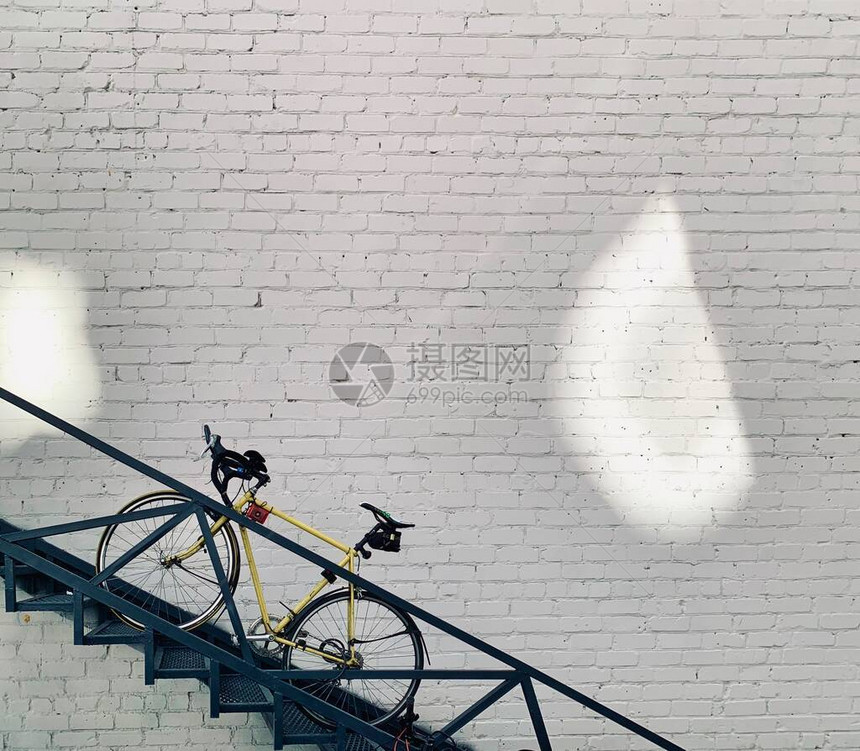 白色砖墙背景楼梯上的黄色男女通用自行车图片