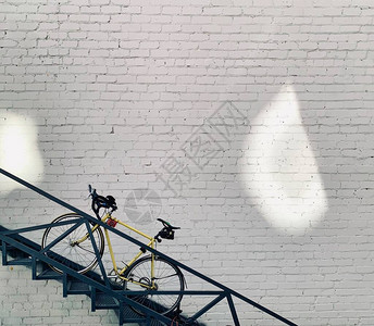 白色砖墙背景楼梯上的黄色男女通用自行车图片