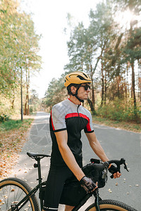 在日落背景下秋天森林的路上骑着自行车站在自行车上的男人的画像图片